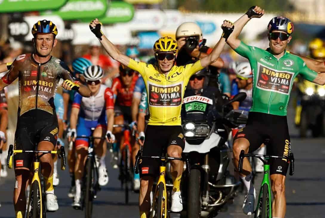Corredores de ciclismo comemorando vitória em uma etapa de corrida de estrada, destaque para ciclistas do team Jumbo Visma e apoiadores.